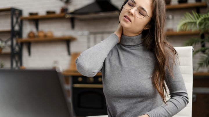 Frau am Schreibtisch mit Nackenschmerzen – ein Beispiel, warum ergonomische Arbeitsplatzgestaltung für gesunde Arbeitshaltung wichtig ist.