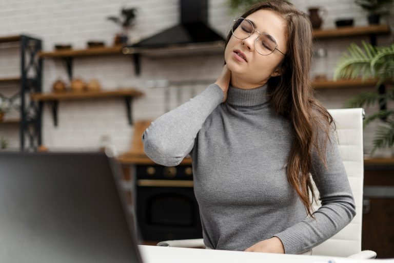 Frau am Schreibtisch mit Nackenschmerzen – ein Beispiel, warum ergonomische Arbeitsplatzgestaltung für gesunde Arbeitshaltung wichtig ist.