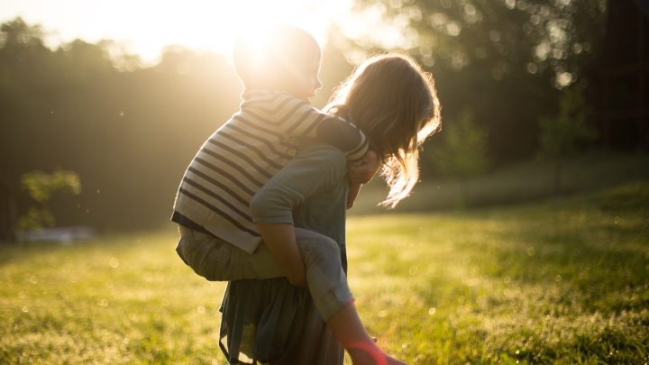 Zwei Kinder spielen draußen im Sonnenlicht. Ein Junge sitzt auf dem Rücken eines Mädchens – eine Szene, die perfekt die Bedeutung von Kinderphysio und motorischer Förderung zeigt.