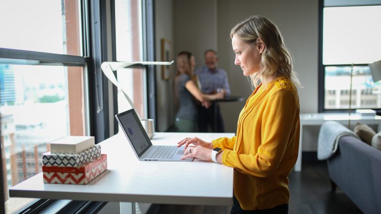 Eine Frau arbeitet an einem Stehschreibtisch – eine ergonomische Arbeitsplatzgestaltung kann bei der Vorbeugung eines Bandscheibenvorfalls helfen.