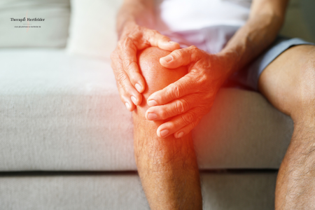 Mann mit Knieschmerzen, Hält sich das knie und sitzt auf dem Sofa